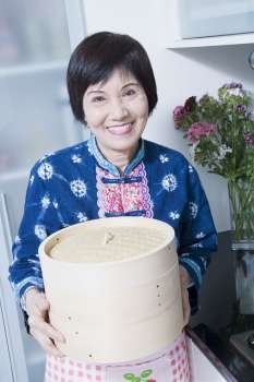Portrait of a senior woman holding a bamboo steamer in a kitchen