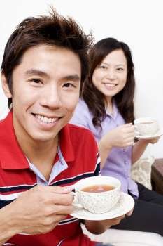 Portrait of a mid adult man drinking a cup of tea with a young woman sitting behind him