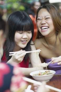 Close-up of two young women eating noodles with chopsticks