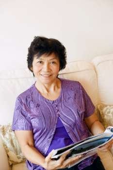 Portrait of a mature woman sitting on a couch and holding a magazine