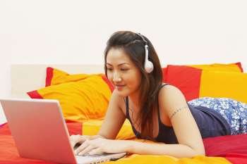 Close-up of a young woman using a laptop and listening to music on headphones