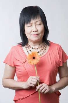 Close-up of a mature woman holding a daisy flower with her eyes closed