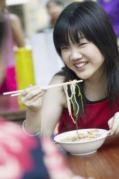 Close-up of a young woman eating noodles with chopsticks
