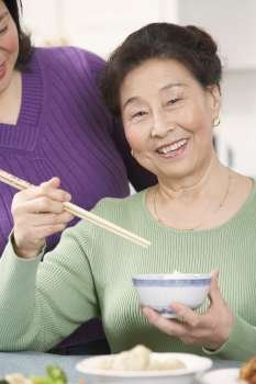 Portrait of a senior woman eating food with her daughter standing behind her