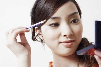 Close-up of a young woman holding a make-up brush and a hand mirror