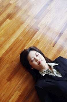 High angle view of a businesswoman lying on the hardwood floor with her eyes closed