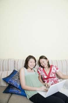 High angle view of two young women smiling and using a laptop