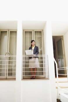 Young woman standing at a doorway of an office and using a laptop