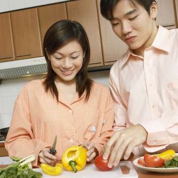 Close-up of a young couple cutting vegetables at a kitchen counter