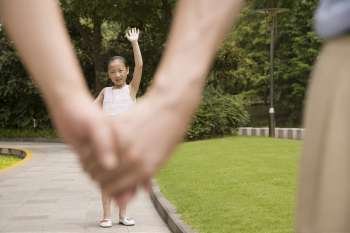 Girl standing in a garden and waving her hand to her parents