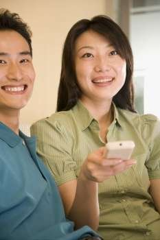 Young woman holding a remote control with a young man sitting beside her and smiling