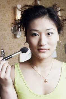 Portrait of a young woman applying make-up on her face