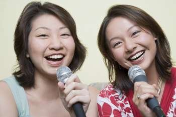 Portrait of two young women singing together into microphones