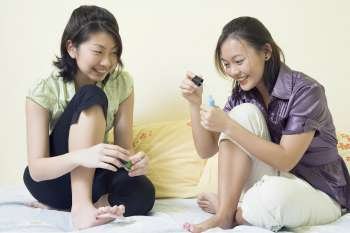 Two young women applying nail polish on their toenails