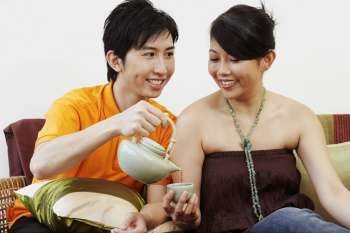 Close-up of a young man pouring coffee in a cup held by a young woman