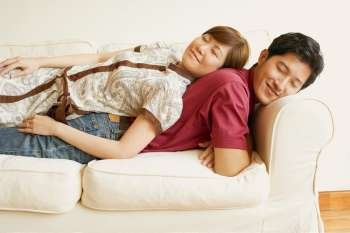 Side profile of a young couple sleeping back to back on a couch