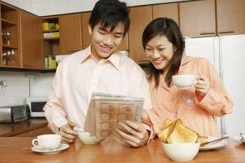 Close-up of a young couple reading a newspaper at a kitchen counter