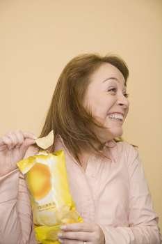Close-up of a mid adult woman holding a packet of potato chips and smiling