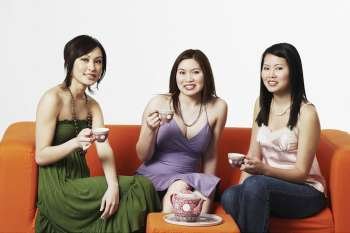 Portrait of three young women sitting on a couch with tea cups