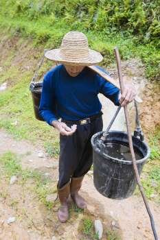 Senior man carrying a buckets full of water on his shoulder, Jinkeng Terraced Field, Guangxi Province, China