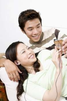 Mid adult man and a young woman lying on a couch and listening to an MP3 player