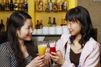 Two young women sitting at a bar counter raising a toast