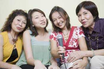 Portrait of two young women singing with their grandmothers into microphones