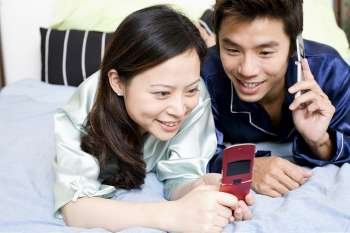 Close-up of a young woman using a mobile phone with a mid adult man lying beside her