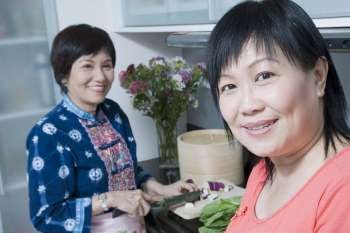 Portrait of a mature woman smiling with her mother cutting vegetables in a kitchen