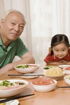 Portrait of a mature man sitting with his granddaughter at a dining table