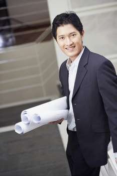 Portrait of a businessman standing on a staircase and holding blueprints