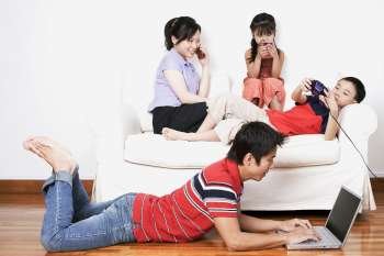 Young woman and her son and daughter sitting on a couch with a mid adult man lying on the floor with a laptop