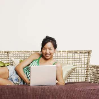 Portrait of a young woman using a laptop on a couch and smiling