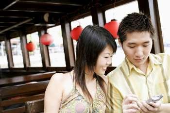 Close-up of a young man using a mobile phone beside a young woman