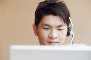 Close-up of a male customer service representative talking on a headset and using a laptop