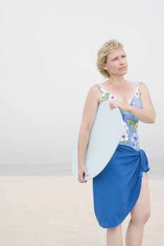 Mature woman standing on the beach and holding a body board