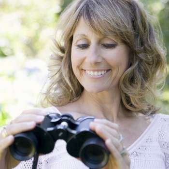 Close-up of a mature woman holding binoculars and smiling