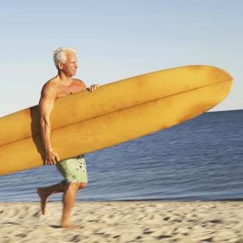 Mature man holding a surfboard and walking on the beach