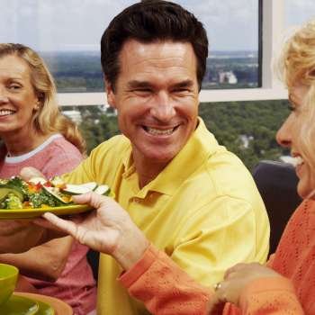 Mid adult woman holding a plate of salad and sitting with a mature couple at the table