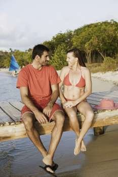 Mid adult couple looking at each other and sitting on a jetty