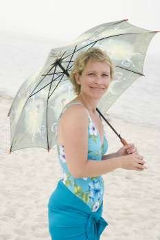 Portrait of a mature woman standing on the beach and holding an umbrella