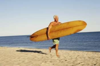 Mature man holding a surfboard and walking on the beach