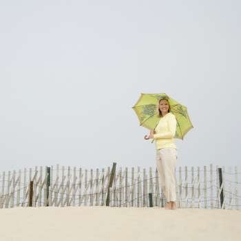 Mid adult woman holding an umbrella and standing near a fence