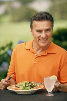 Portrait of a mature man sitting at the table with a plate of vegetable salad in front of him