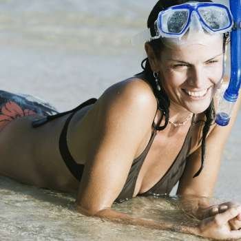 Mid adult woman wearing snorkeling gear and lying on the beach