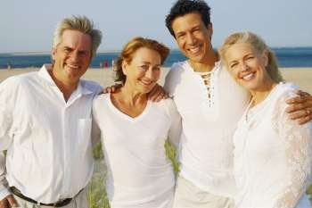 Portrait of two mature couples standing with their arms around each other on the beach