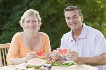 Portrait of a mature couple sitting at a table and holding slices of watermelon