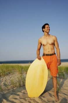 Mature man standing on the beach and holding a wooden surfboard