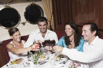 Two mid adult couples toasting with wine glasses and smiling