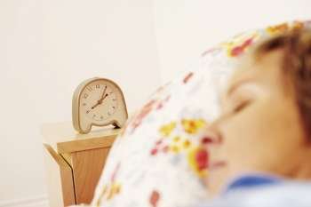 An alarm clock beside a mature woman sleeping on the bed